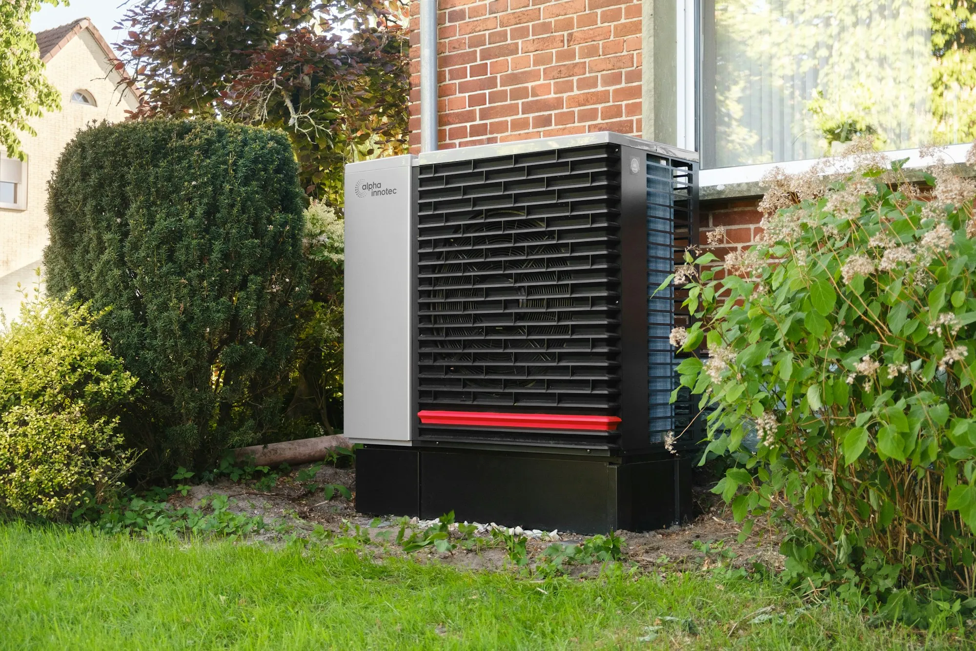 Moderne Außen-Wärmepumpe an einer sanierten Backstein-Hauswand.